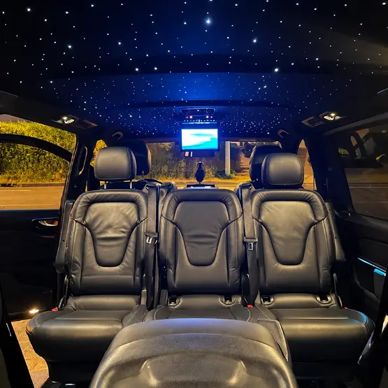 Intérieur d’un van avec sièges en cuir noir, écran et plafond étoilé éclairé en bleu.