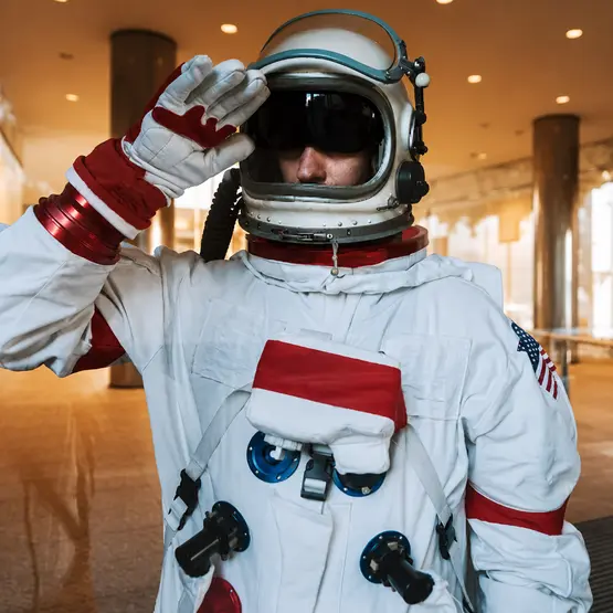 Une personne en combinaison spatiale blanche et casque salue.